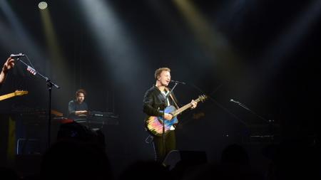 Ein Mann mit Gitarre steht auf einer Bühne und singt in ein Mikrofon.
